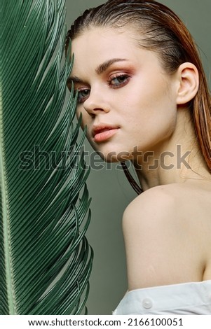 a sophisticated, elegant woman with evening makeup, stands with a green palm leaf, covering part of her face with it. Close vertical portrait, photo without retouching. High quality photo