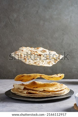Homemade Indian flat bread Chapati or Roti on grey concrete background. Creative photography with levitation. Royalty-Free Stock Photo #2166112957