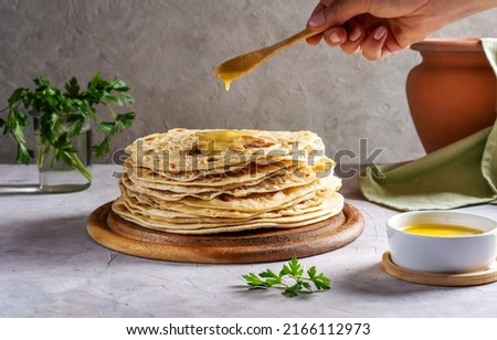 Homemade Indian Chapati or Roti on grey concrete background with human hand pouring butter ghee over  Royalty-Free Stock Photo #2166112973