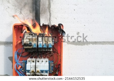 Burning switchboard from overload or short circuit on wall. Circuit breakers on fire and smoke from overheating due to poor connection. Dangerous home electrical wiring concept, copy space Royalty-Free Stock Photo #2166152535