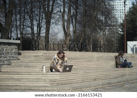 Young college student sitting outdoors and working on a laptop comuter.