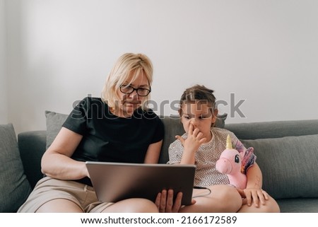 Granny and preschool girl using tablet together at home on the sofa, family togetherness time 