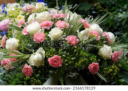 pastel funeral flowers on a grave in front of a wooden cross in blurred background