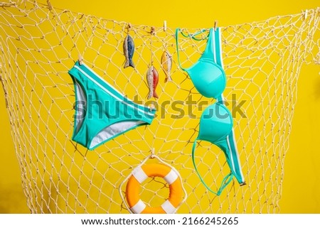 A green swimsuit and wooden fish with a lifebuoy hang on a fishing net on a yellow background