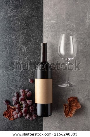 Red wine with grapes on a stone background. On a bottle empty label. Top view.