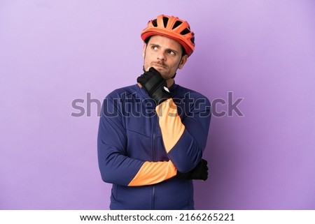 Young Brazilian cyclist man isolated on purple background having doubts and thinking