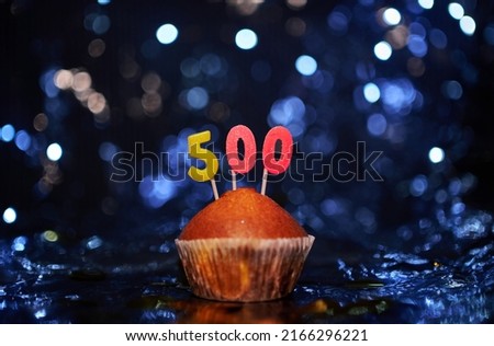 Digital gift card birthday concept. Tasty fresh vanilla anniversary cupcake with number 500 five hundred on aluminium foil and blurred bright background in minimalistic style. High quality image