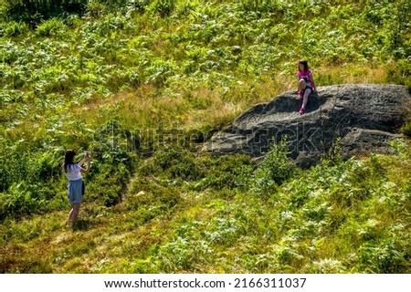 a teenage girl taking picture of her small sister on the big stone in the forest