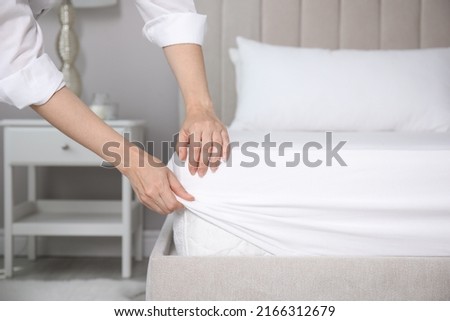Woman putting white fitted sheet over mattress on bed indoors, closeup Royalty-Free Stock Photo #2166312679