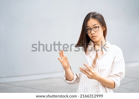 Portrait of young Asian Thai, Vietnamese or Chinese woman in shirt and glasses standing outside near office using tablet with cam reading working, learning or chatting. Education, wireless technilogy