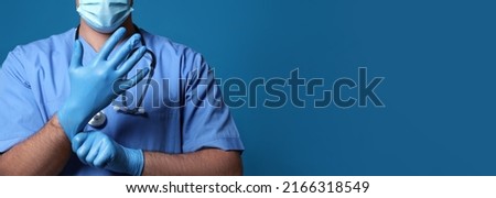 Surgeon putting on medical gloves against blue background, closeup. Banner design with space for text Royalty-Free Stock Photo #2166318549