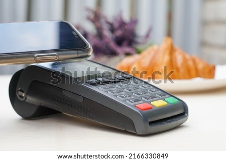 Close up of young woman pays the purchase through the smartphone at bakery. Bank payment terminal. NFC technology.
