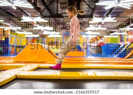 Cute girl kid jumping on trampoline and happy at playground park. Caucasian child in motion during active entertaiments Royalty-Free Stock Photo #2166359557