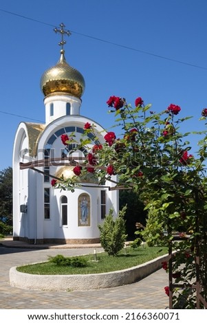 Blooming bush with red roses close to the Orthodox Church. The dome of the church glistens in the sun, reflects sunlight. Power lines cross the frame. The picture was taken on a sunny summer day.