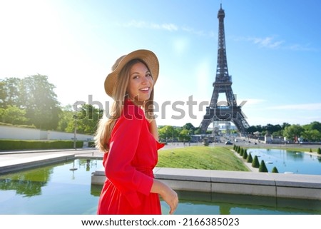 Holidays in Paris. Elegant lady in red dress and hat smiling at camera with Eiffel Tower on the background.