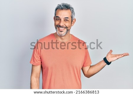 Handsome middle age man with grey hair wearing casual t shirt smiling cheerful presenting and pointing with palm of hand looking at the camera. 