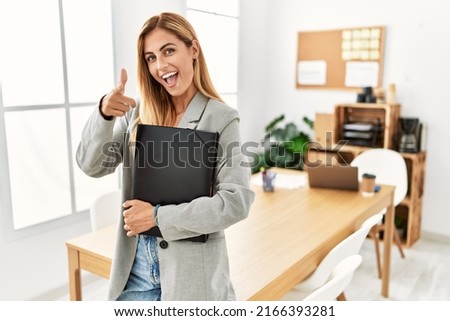 Blonde business woman at the office pointing fingers to camera with happy and funny face. good energy and vibes.  Royalty-Free Stock Photo #2166393281