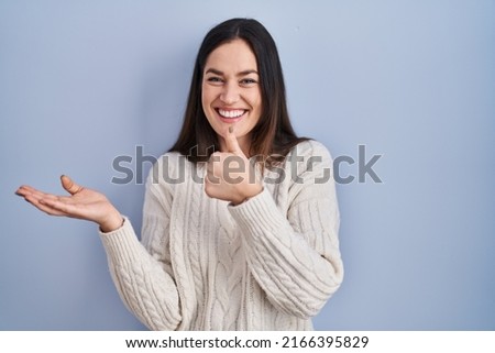 Young brunette woman standing over blue background showing palm hand and doing ok gesture with thumbs up, smiling happy and cheerful  Royalty-Free Stock Photo #2166395829
