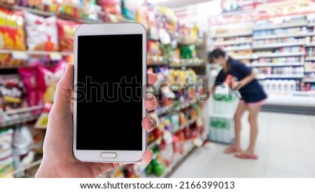 Woman use mobile phone,blur image of a girl choosing snacks in a convenience store as background. Royalty-Free Stock Photo #2166399013