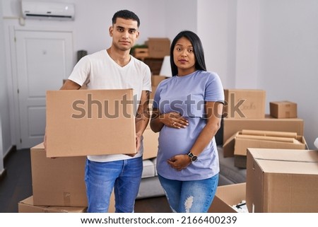 Young hispanic couple expecting a baby moving to a new home relaxed with serious expression on face. simple and natural looking at the camera. 
