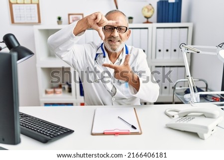 Mature doctor man at the clinic smiling making frame with hands and fingers with happy face. creativity and photography concept. 
