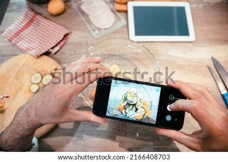 Male hands photographing vegetables while preparing vegetarian food and blogging online using smartphone. Sharing Photo massage to social network of fresh salad. Cut out image, close up