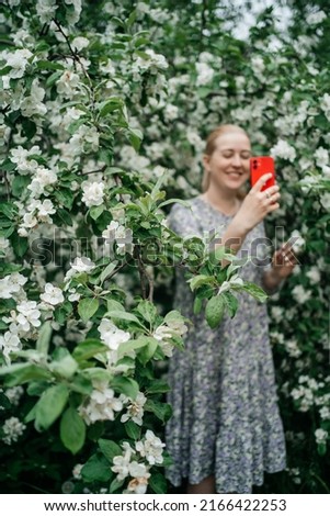 girl in blooming apple tree using smartphone video call outdoor nature