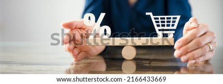 Human Hand Protecting Balance Between Red Percentage Cubic Block And Shopping Cart On Wooden Seesaw Royalty-Free Stock Photo #2166433669