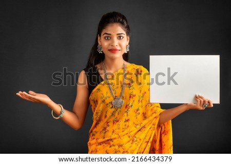 A young girl or businesswoman wearing a saree and holding a signboard in her hands on a gray background.
