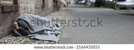 Homeless Man Covered With Blanket Sleeping On Street In City Royalty-Free Stock Photo #2166435055