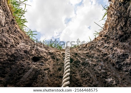 Looking up from hole in ground with rope. Lifeline, debt, mental health help concept.  Royalty-Free Stock Photo #2166468575