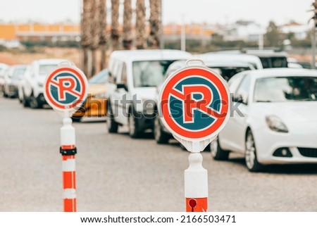 A sign prohibiting parking and stopping cars near the entrance to the shopping center. Lots of rule-breaking cars in the background
