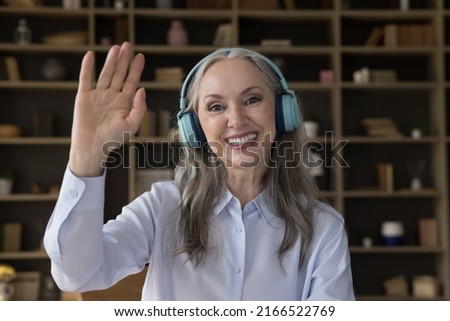 Head shot portrait happy older 55s woman wear wireless headphones staring at camera, greeting client or friend makes video conference call, web cam face view. Virtual meeting event by business concept Royalty-Free Stock Photo #2166522769