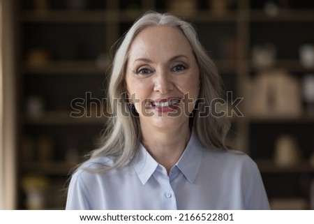 Head shot of middle-aged attractive businesswoman standing in office posing for cam, having wide candid toothy smile staring at camera feels happy. Portrait of baby boomer generation female concept