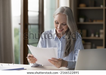 Smiling middle-aged businesslady read paper notification, letter, correspondence get good business news looks satisfied with sales growth, busy in paperwork in modern office. Success, advance concept Royalty-Free Stock Photo #2166522895