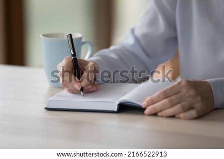 Close up middle-aged woman sit at desk write in paper planner, create important notes or meetings not to forget, jotting business plans and tasks memos. Week goals, to-do list, time management concept Royalty-Free Stock Photo #2166522913
