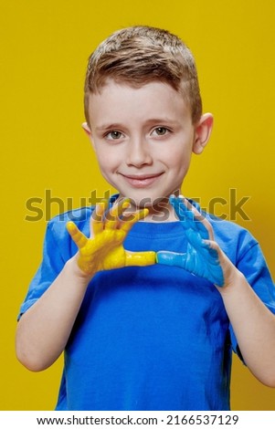 Little happy boy with painted palms in yellow and blue, the colors of the flag of Ukraine. Ukrainian creative preschooler.