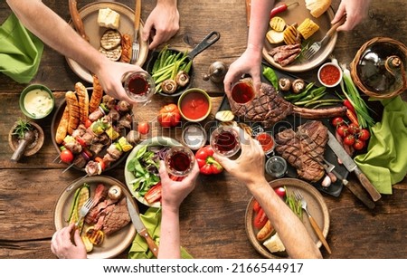 Friends having a barbecue party. Group of people eating grilled meats and vegetables and drinking wine at rustic picnic table Royalty-Free Stock Photo #2166544917