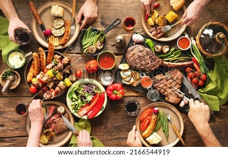 Friends having a barbecue party. Group of people eating grilled meats and vegetables and drinking wine at rustic picnic table Royalty-Free Stock Photo #2166544919