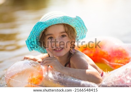 Girl in a hat stands on the river bank with a transparent inflatable circle in the shape of a heart with orange feathers inside. Beach holidays, swimming, tanning, sunscreens.