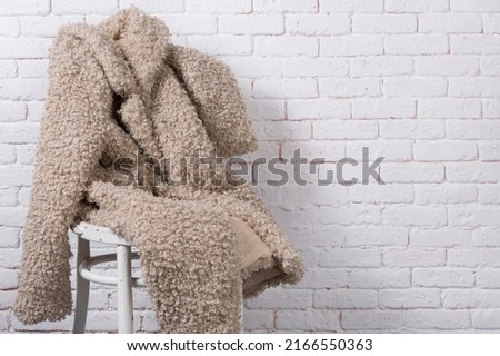 beige faux fur coat, as if sitting on a chair against a white brick wall, copy spase Royalty-Free Stock Photo #2166550363