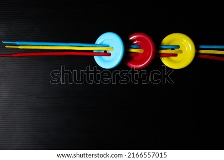 Taking photo of three buttons and nylon rope in blue red and yellow colour on dark background.