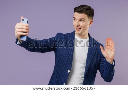 Young employee business man lawyer 20s wear formal blue suit white t-shirt work in office do selfie shot on mobile cell phone meet greet wave hand isolated on pastel purple background studio portrait.