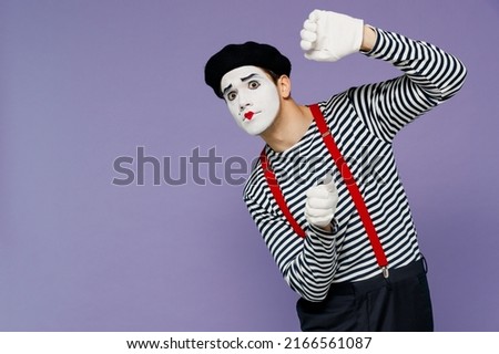 Charismatic amazing marvelous ecstatic young mime man with white face mask wears striped shirt beret looking from behind invisible wall isolated on plain pastel light violet background studio portrait