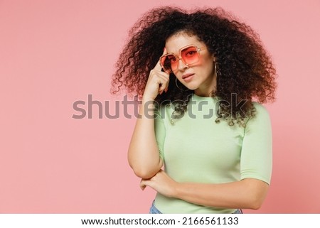 Preoccupied fatigued distempered unnerved young curly latin woman 20s years old wears mint t-shirt sunglasses put index finger on temple isolated on plain pastel light pink background studio portrait Royalty-Free Stock Photo #2166561133