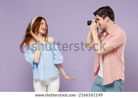 Two fun traveler tourist woman man couple in shirt taking photo portrait of girlfriend by camera isolated on purple background Passenger travel abroad on weekends getaway Air flight journey concept Royalty-Free Stock Photo #2166561149