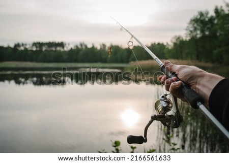 Fishing for pike, and perch from a lake or pond. Background wild nature. Fisherman with rod, spinning reel on the river bank. Wild nature. The concept of a rural getaway. Article about fishing day. Royalty-Free Stock Photo #2166561633