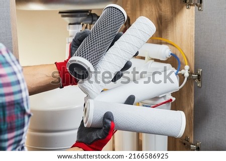 Water filter cartridge in human hand. Plumber hands holding cartridge for replace a water filter at kitchen. Fix purification osmosis system. Royalty-Free Stock Photo #2166586925