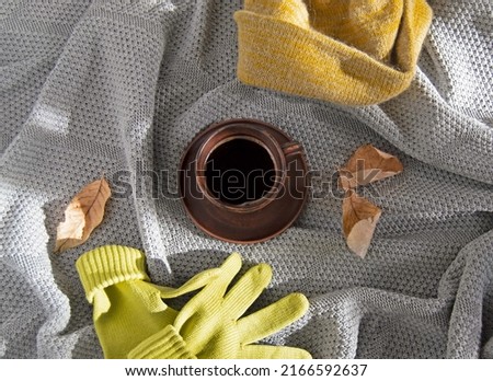 Gray knitted blanket, yellow knitted gloves, yellow woolen hat, clay coffee mug. Top view. Autumn concept.