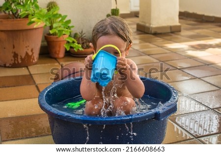 Boy getting wet in summer in a plastic bathtub, he is playing splashing with water in the garden at home. Vacation lifestyle at home.  Baby playing